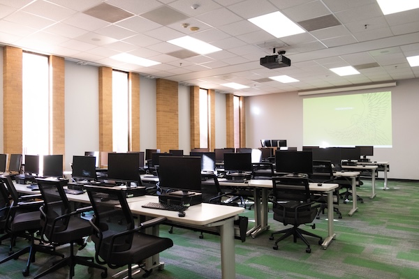 computer classroom with computer stations and presentation screen as seen from rear-right